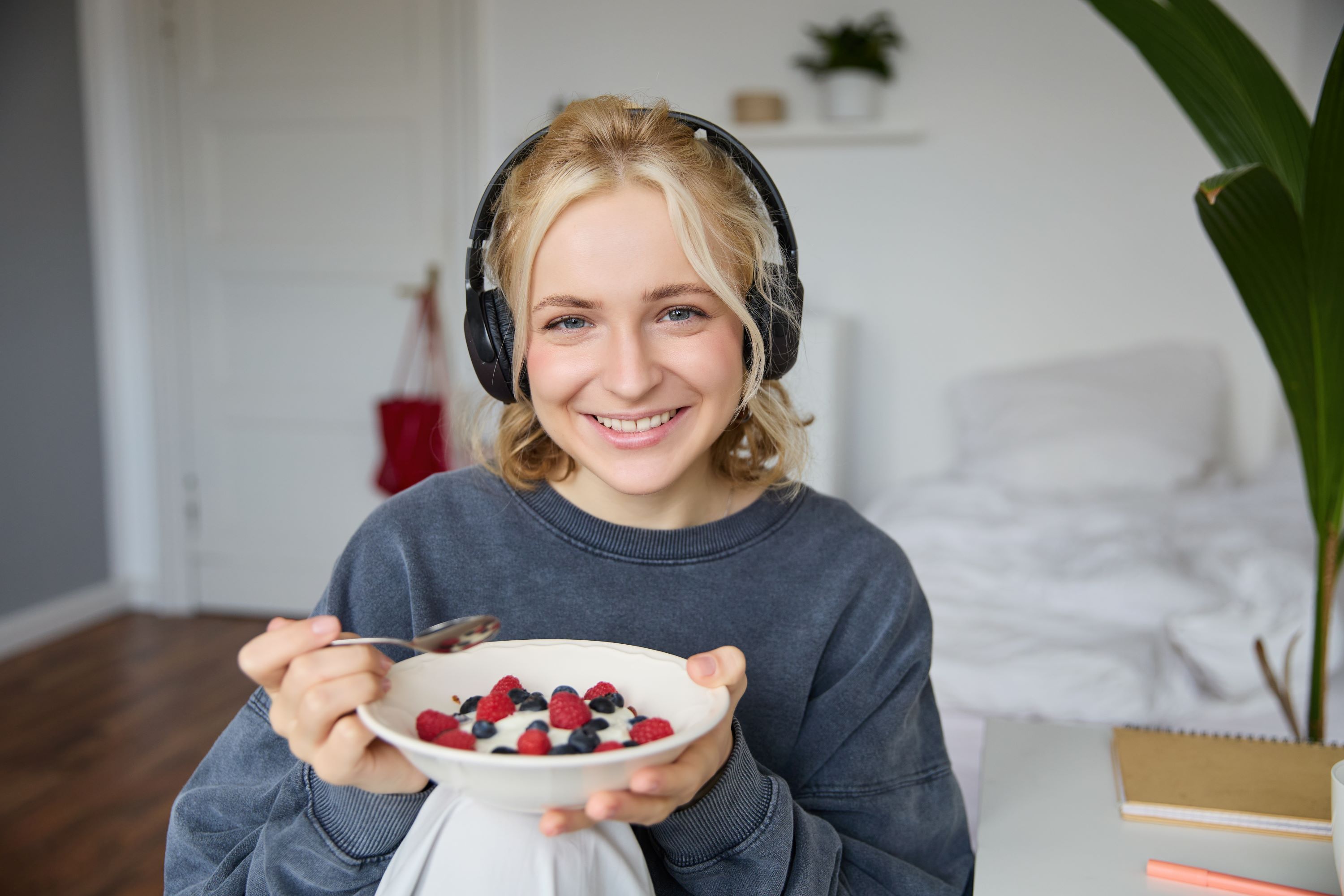 portrait smiling cute woman headphones eating her breakfast watching video laptop